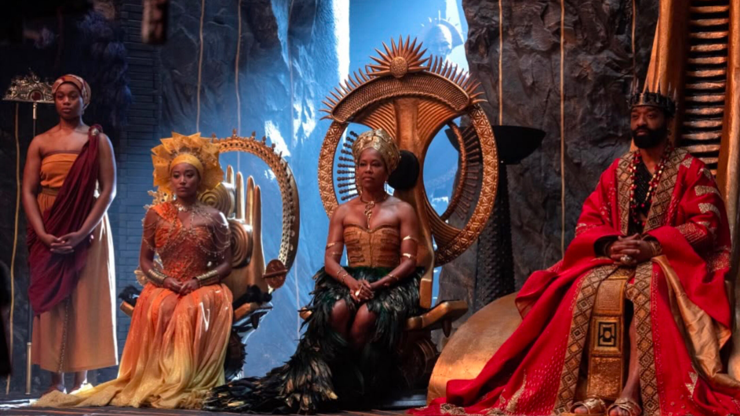 A regal scene from the upcoming film Children of Blood and Bone, showing Viola Davis and Idris Elba seated on ornate thrones in a grand royal court, dressed in elaborate traditional-inspired royal attire alongside other cast members in a majestic fantasy setting.