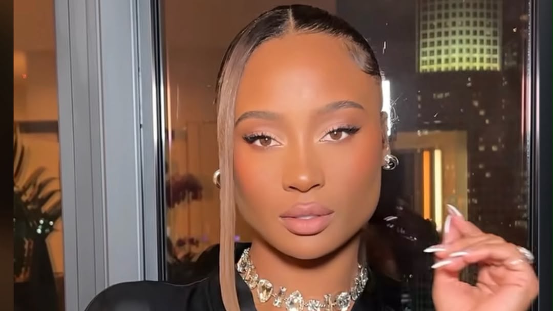 Close-up portrait of Kayla Nicole in a glamorous look with sleek hair and bold makeup, photographed against a city skyline at night.